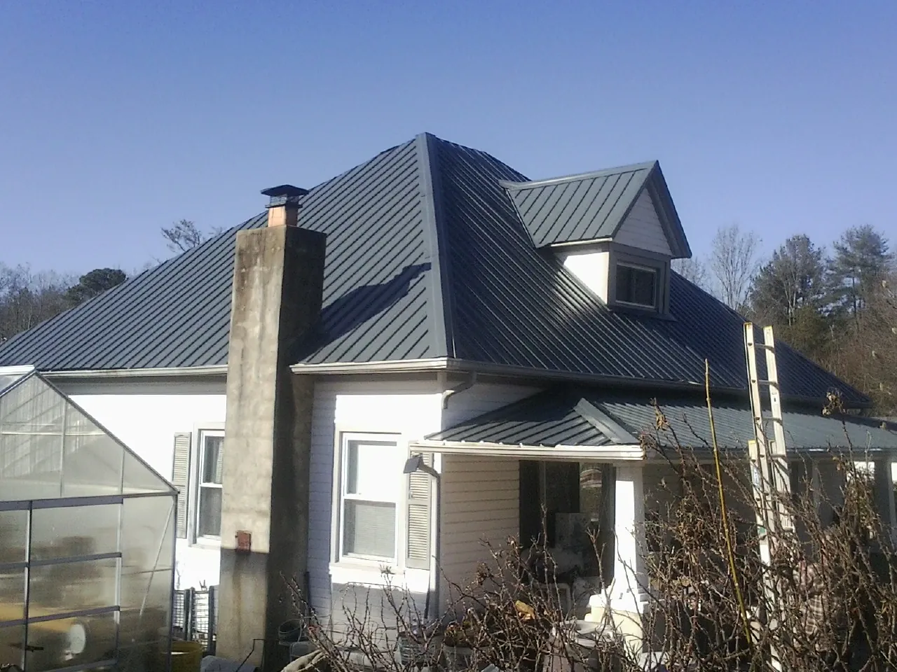 Dark blue standing seam metal roof on a white farmhouse with dormer — Slate & Tile Roof Repair by Roofing Brothers in Canmer