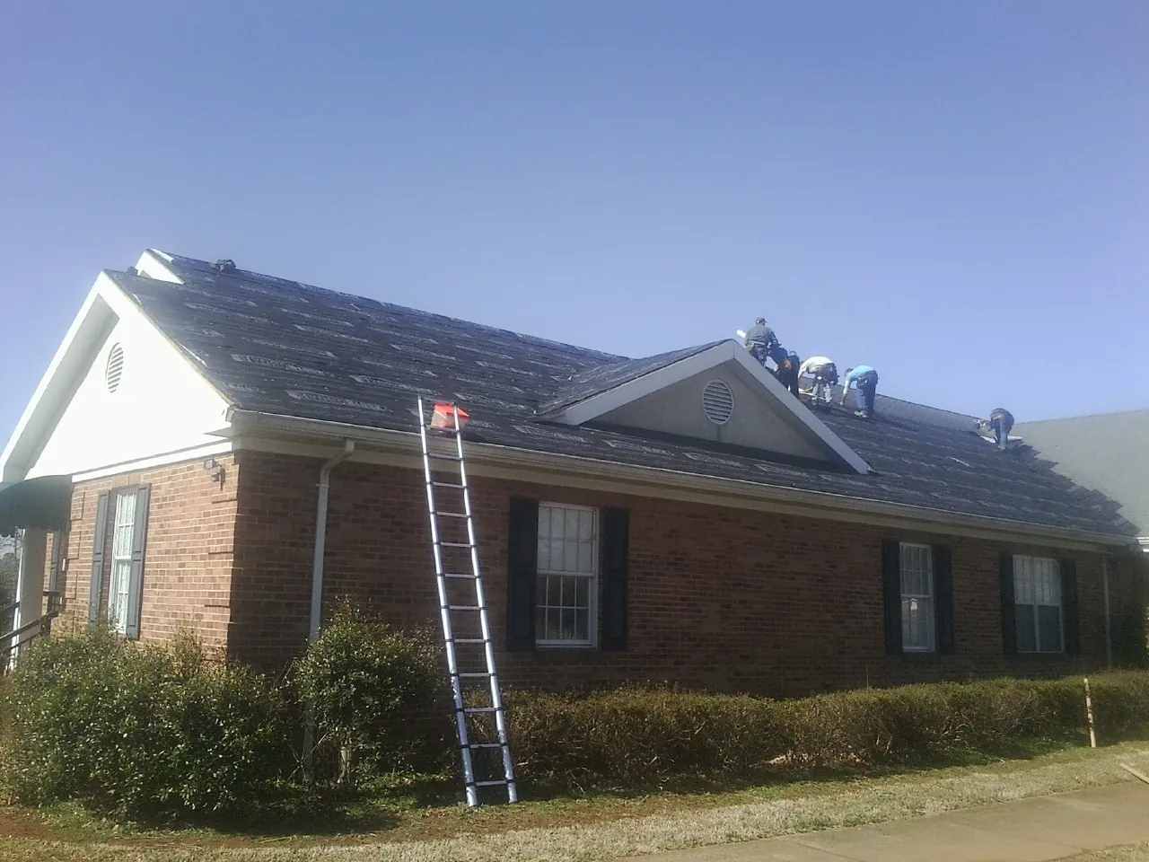 Crew tearing shingles off a brick ranch roof with a ladder set — Metal Roof Repair work by our crew in Canmer