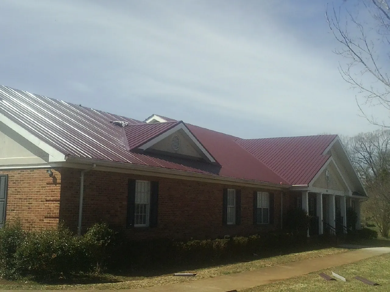Red metal roof with gabled entries on a long brick building, from a Hail Damage Roof Repair job in Canmer