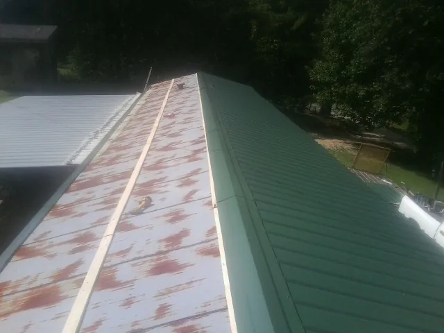 Old rusted panels beside newly installed green metal roofing — Wind Damage Roof Repair by Roofing Brothers in Canmer