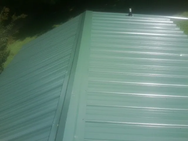 New green metal panels meeting at the ridge of a roof — Flat Roof Repair work by our crew in Canmer