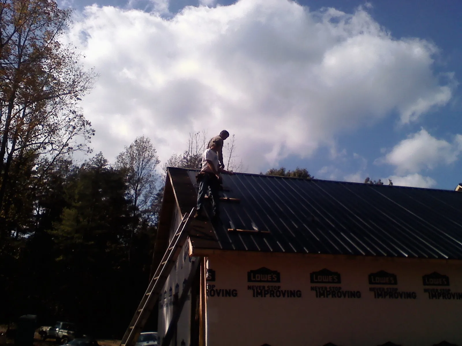 Roofer fastening dark metal panels high against a cloudy sky, from a Roof Inspection job in Canmer