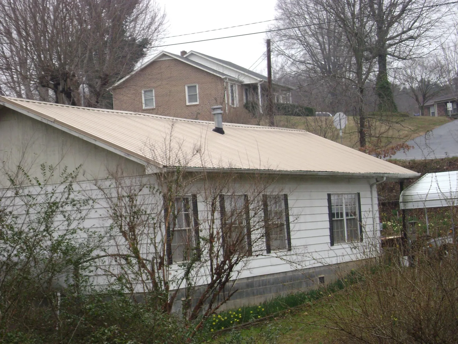 Tan metal roof on a white sided house set into a hillside — Commercial Roofing by Roofing Brothers in Canmer